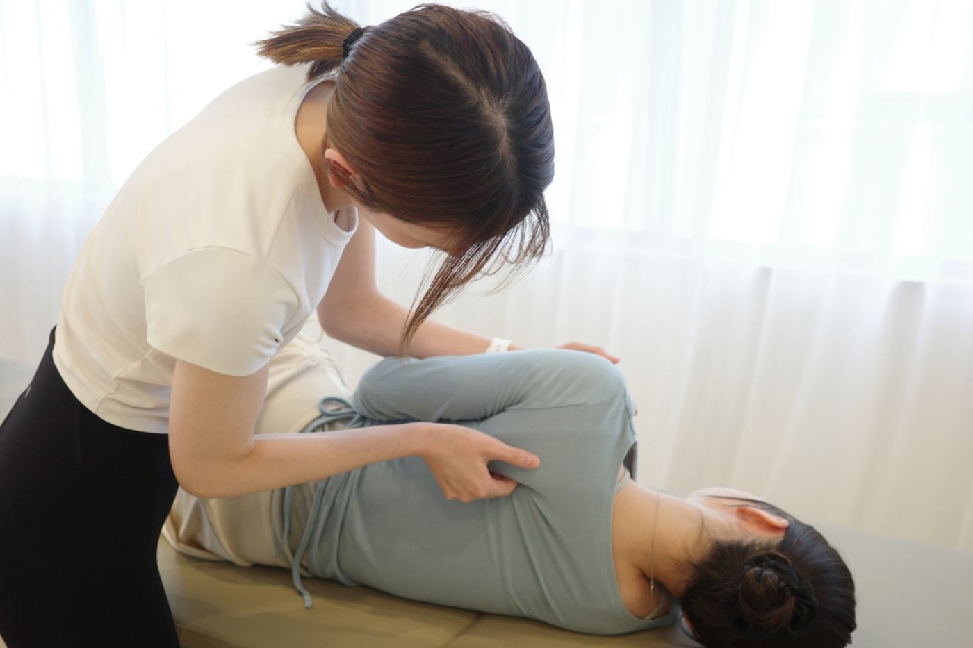 横向きに寝たお客様の背中から腰にかけて、インストラクターが手で筋膜に圧をかけている